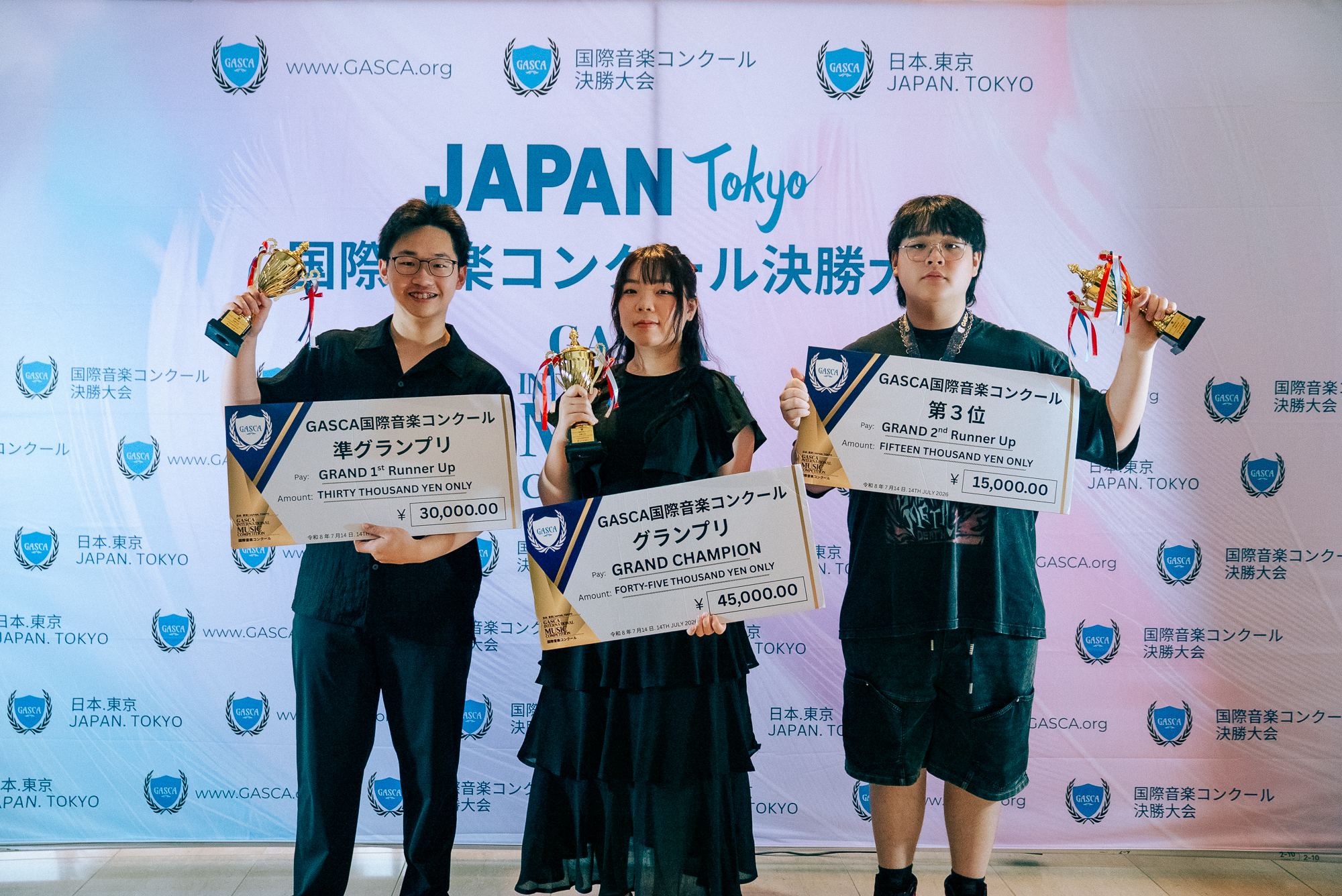 Three Tokyo finalists posing with trophies and giant cash-prize cheques