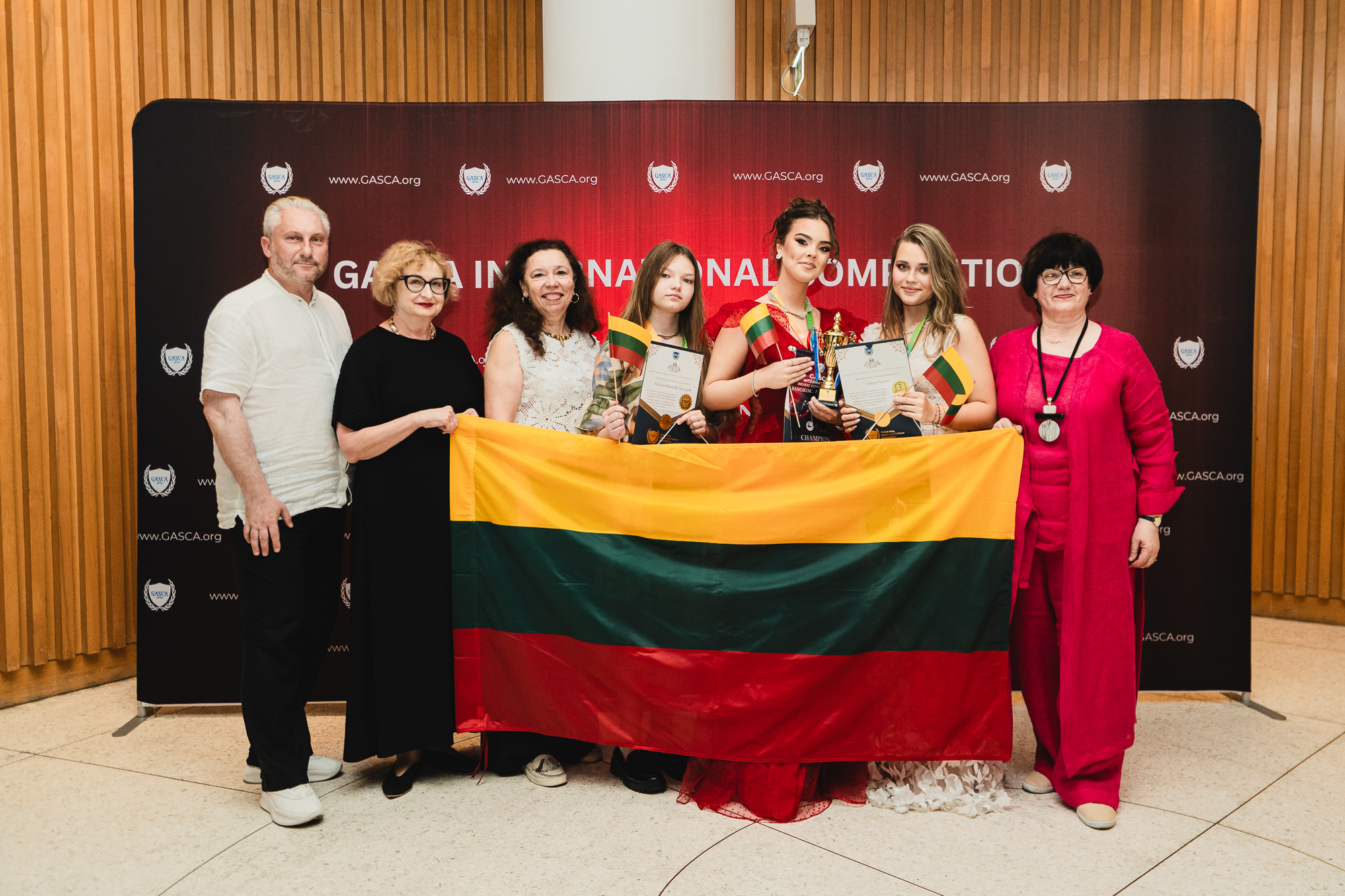 Group of participants holding the Lithuanian flag with medals and trophies
