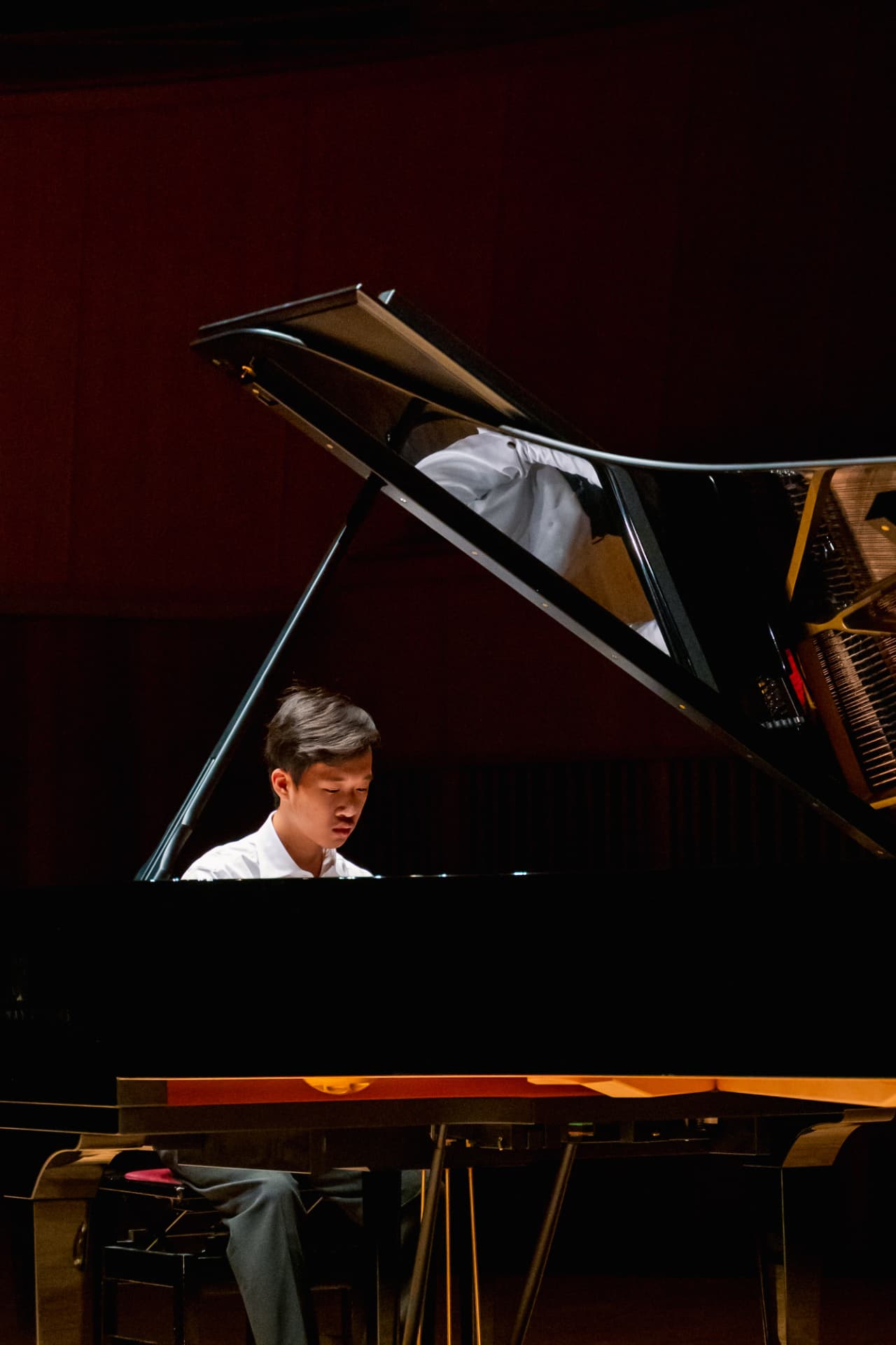 Pianist performing on a grand piano under warm stage light