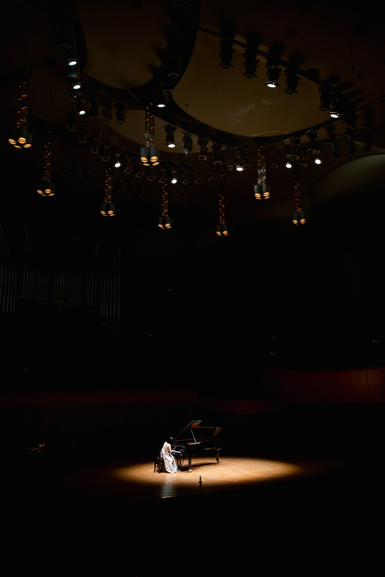 Pianist in a white gown beneath the concert hall lighting rig