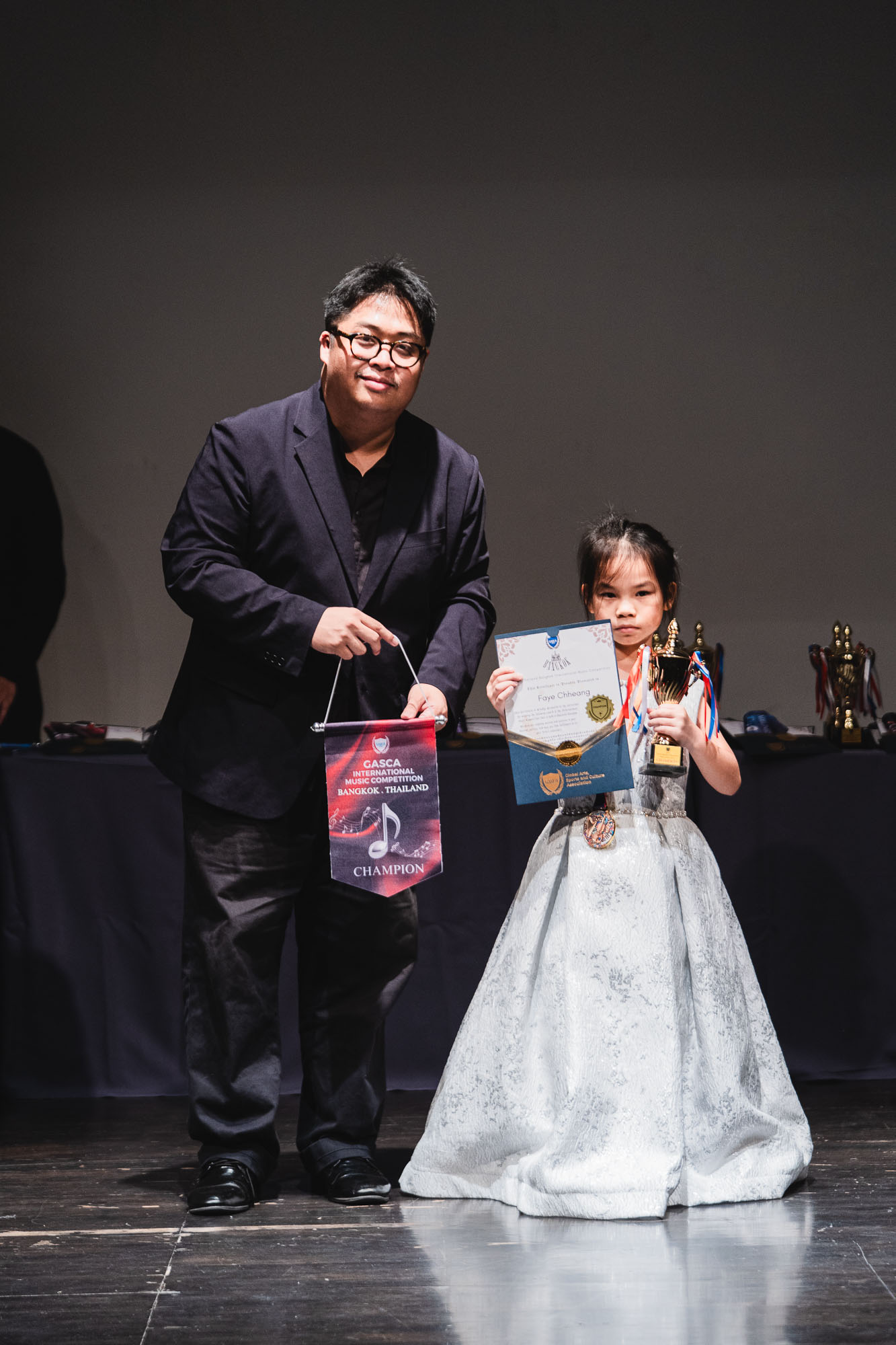 Young winner in a white gown with trophy and champion pennant