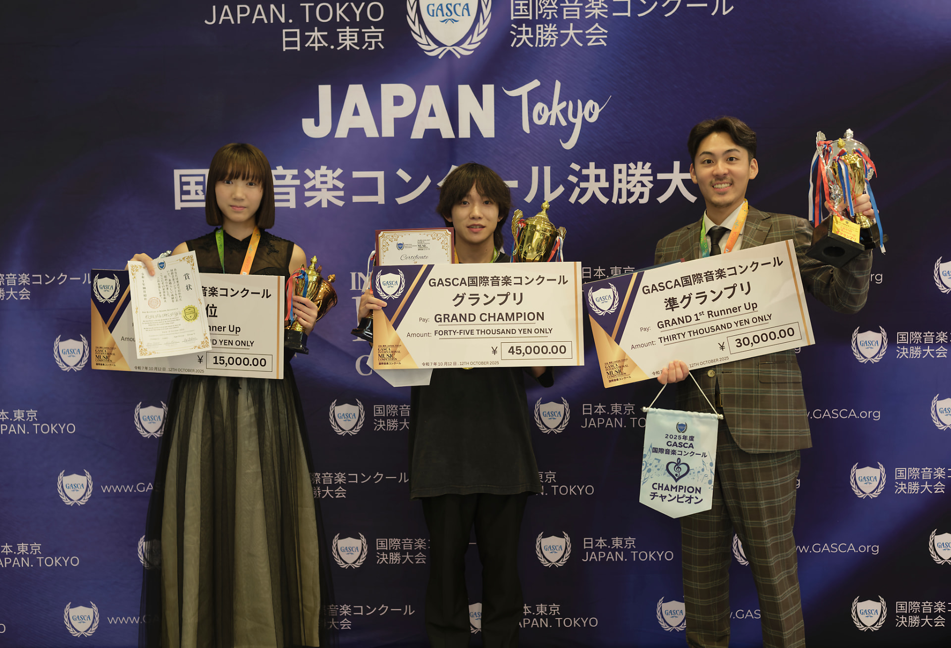 Three Tokyo competition winners holding trophies, certificates and giant prize cheques